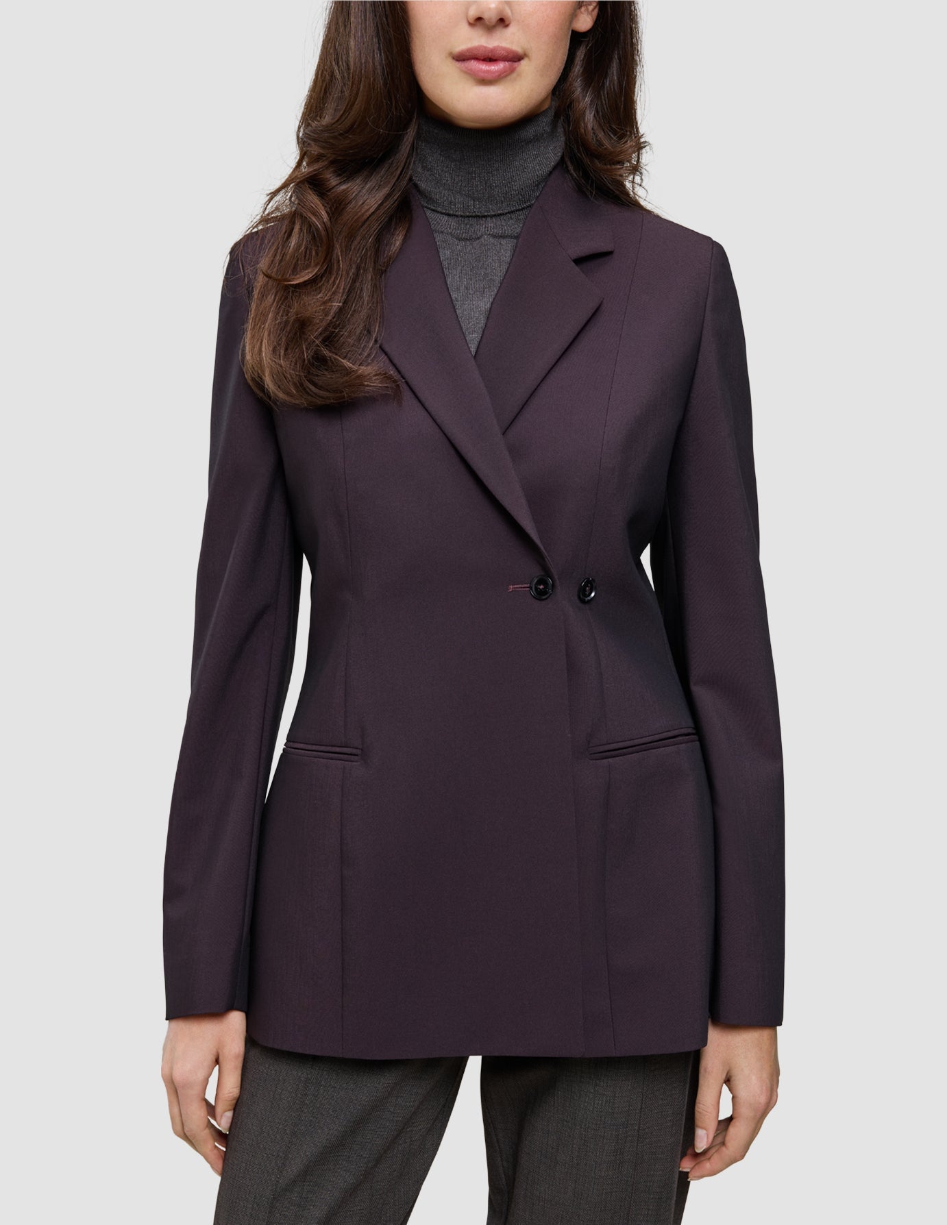 A person wearing a dark burgundy Women’s Avira Blazer Burgundy Berry double-breasted blazer over a gray turtleneck sweater.