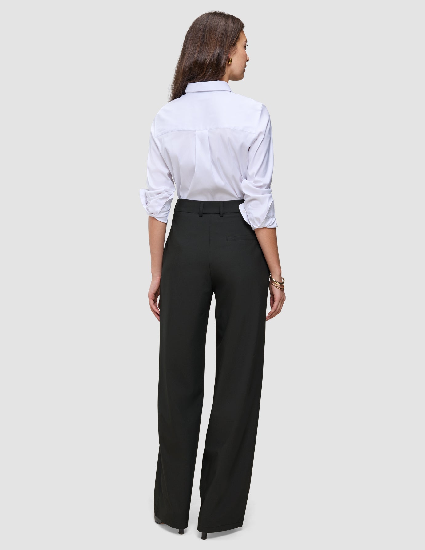 Back view of a person wearing a white collared shirt and black Women’s Avira Pants Wide, featuring a high-waisted, wide-leg Scandinavian design.