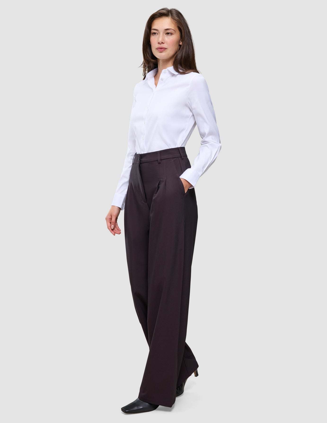 A woman wears a white button-down shirt tucked into high-waisted, wide-fit Women’s Avira Pants Wide Burgundy Berry.