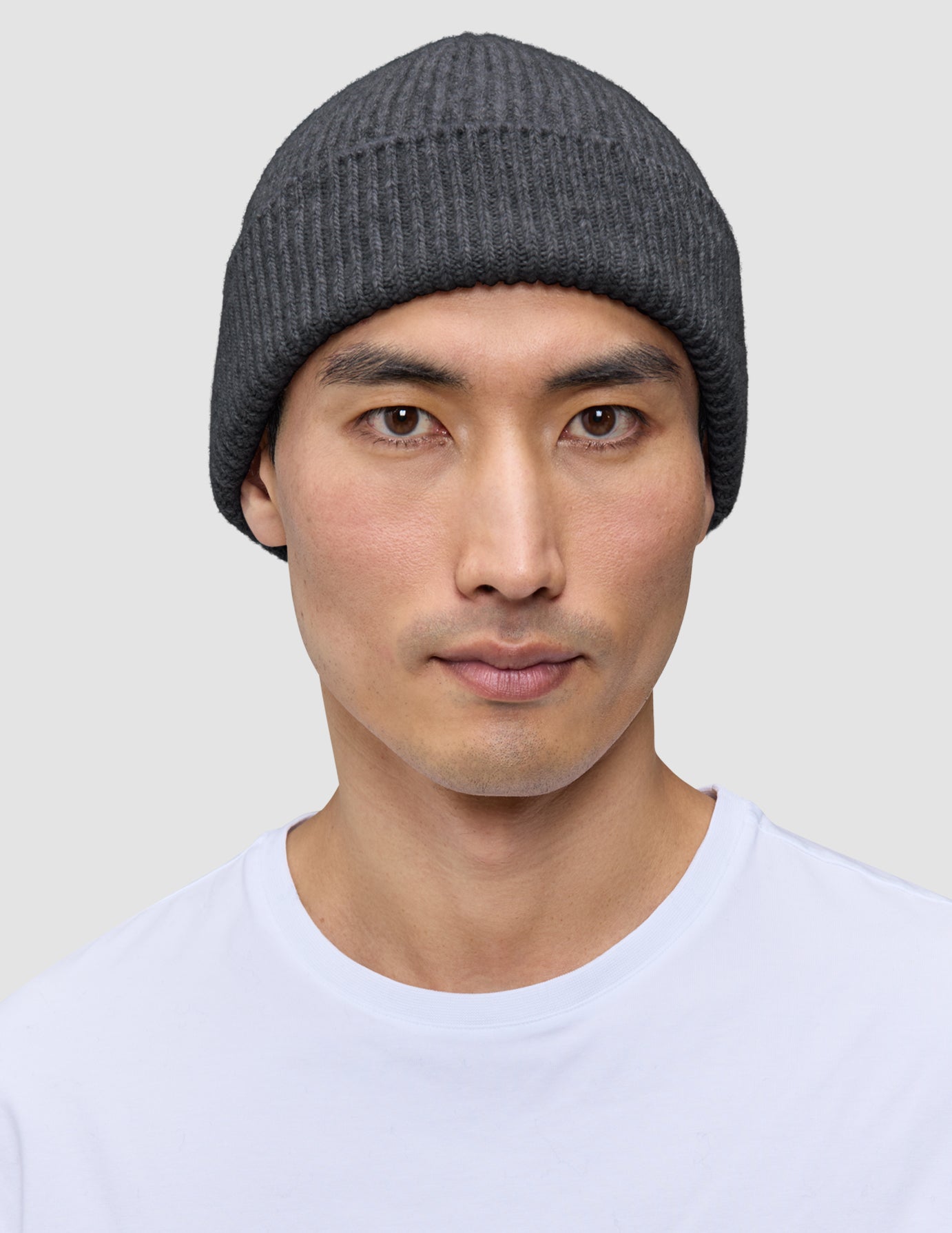 A person wearing a dark grey merino wool rib knit Beanie Dark Grey.