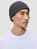 A person wearing a dark grey merino wool rib knit Beanie Dark Grey.