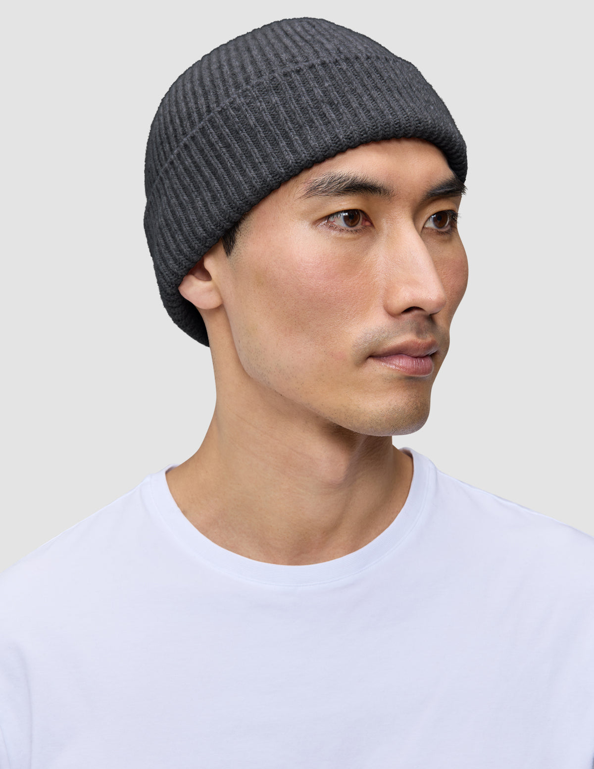 A person wearing a dark grey merino wool rib knit Beanie Dark Grey.