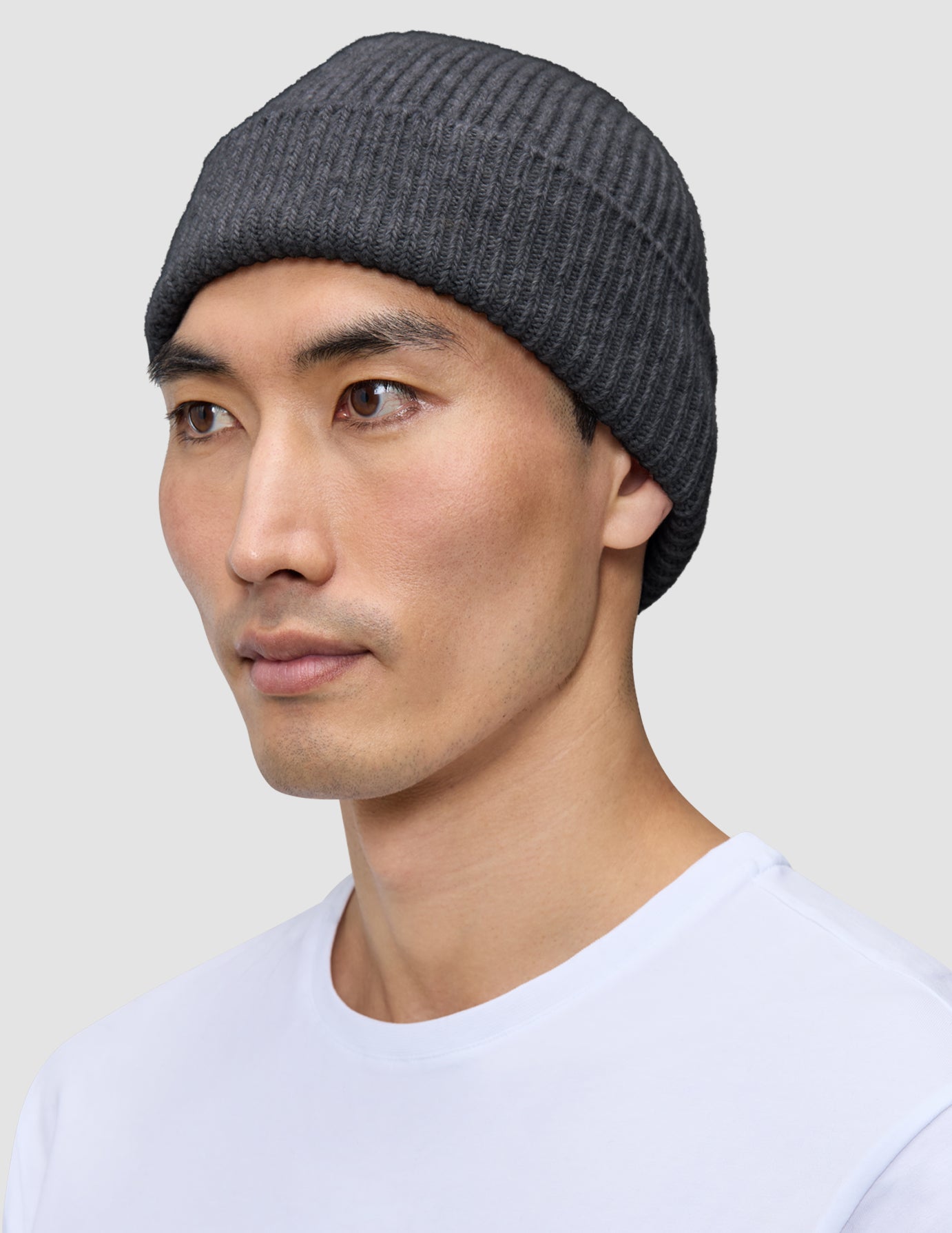 A man wearing a dark grey merino wool rib knit Beanie Dark Grey.