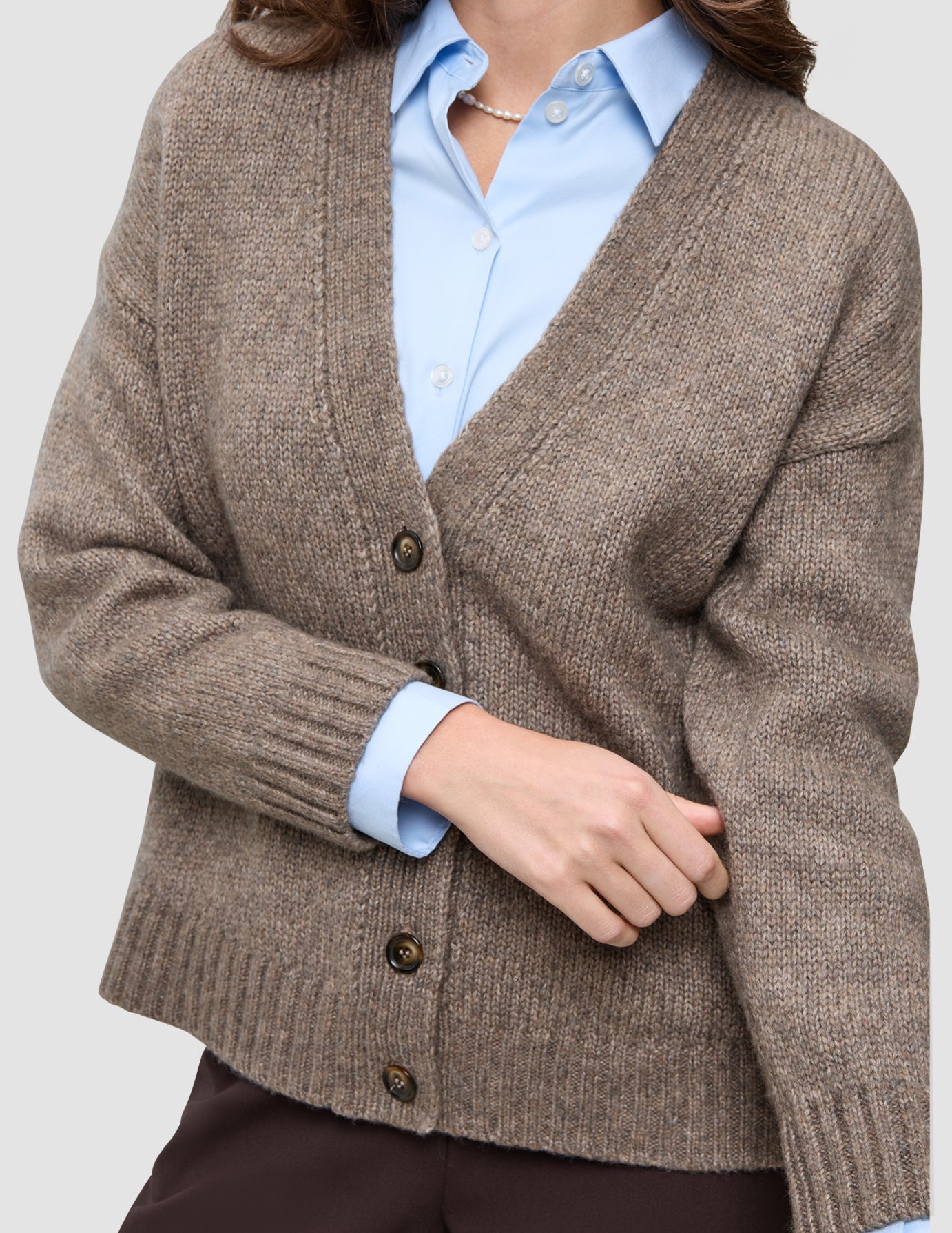 A person wearing a Women’s Chunky Soft Wool Knit Cardigan Taupe Melange over a light blue collared shirt and a string of pearls.