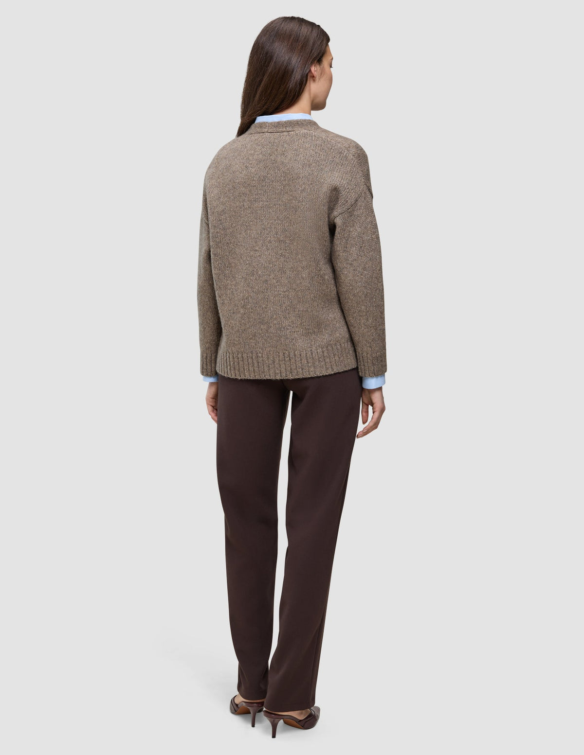A person wearing a Women’s Chunky Soft Wool Knit Cardigan Taupe Melange over a light blue collared shirt and dark brown trousers.