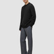 A man wears a Chunky Soft Wool Knit Crewneck Black sweater of Scandinavian design with grey trousers.