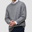 A person wearing a Chunky Soft Wool Knit Crewneck Glacier Grey over a white collared shirt and dark trousers.
