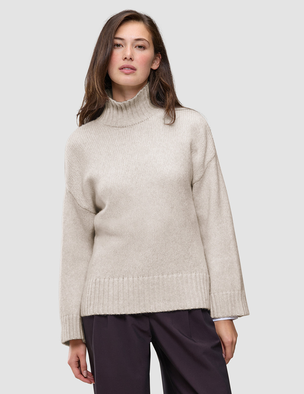A woman wearing the Women’s Chunky Soft Wool Knit Turtleneck Sugar Melange, an oversized, light beige merino wool sweater with ribbed cuffs and hem in a minimalist Scandinavian design.