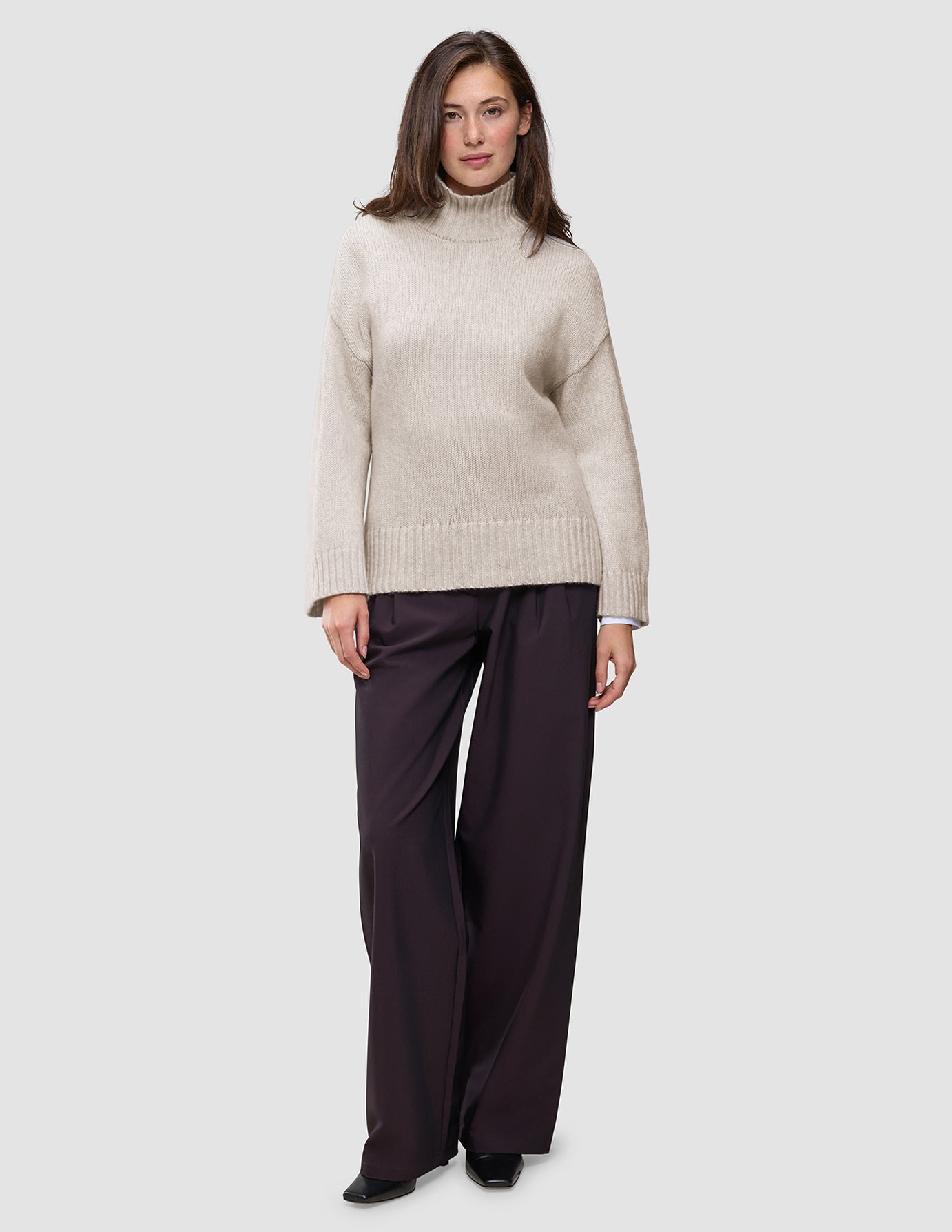 A person wearing a Women’s Chunky Soft Wool Knit Turtleneck Sugar Melange in beige and dark wide-leg trousers.