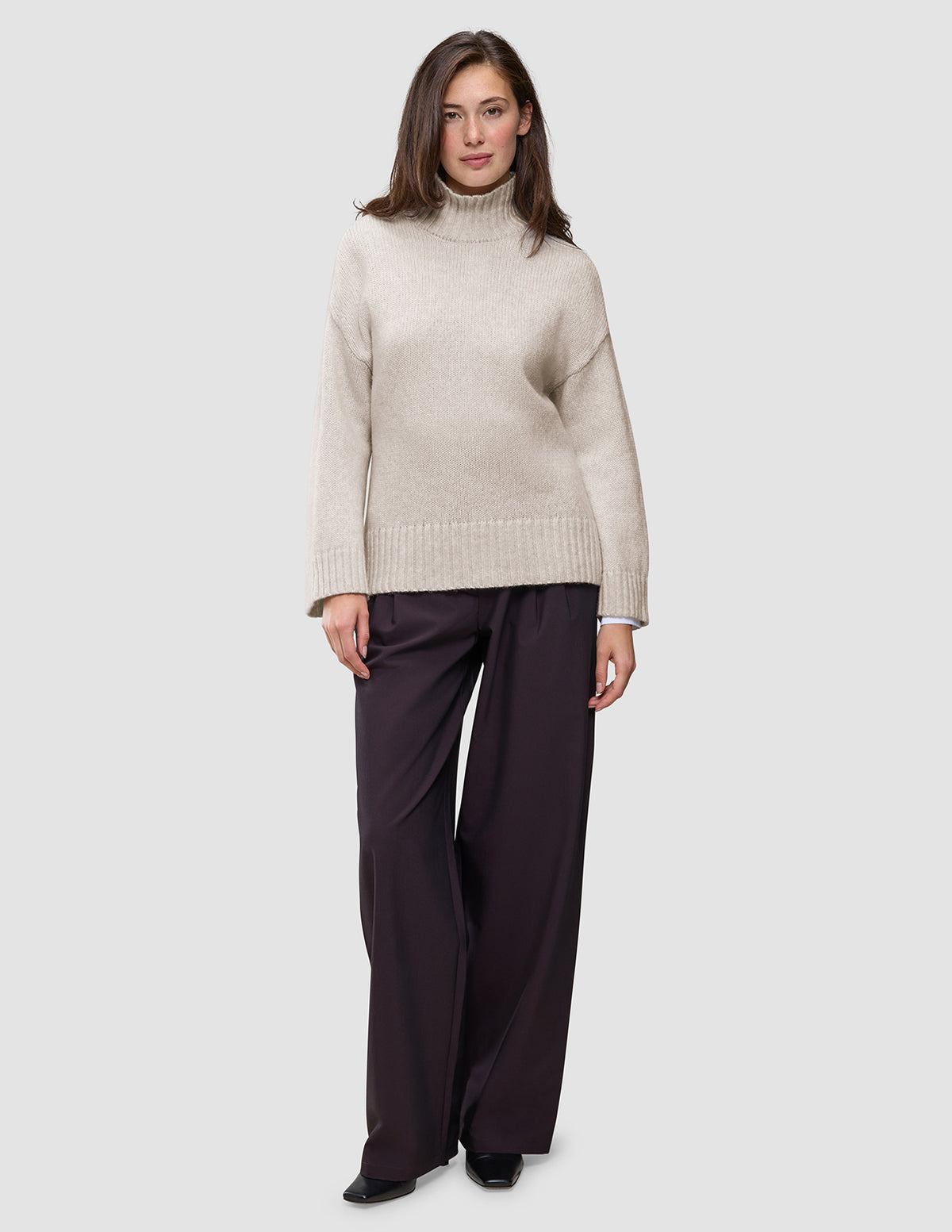A person wearing a Women’s Chunky Soft Wool Knit Turtleneck Sugar Melange in beige and dark wide-leg trousers.