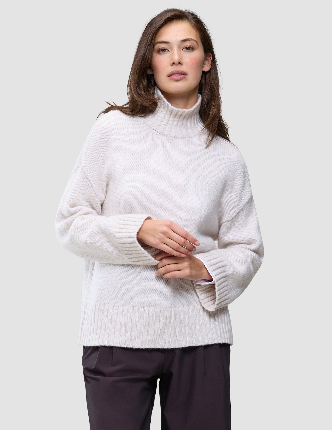 A woman wearing a Women’s Chunky Soft Wool Knit Turtleneck Sugar Melange, an oversized cream-colored chunky wool turtleneck sweater with wide sleeves and ribbed trim.