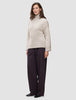 A woman wears a Women’s Chunky Soft Wool Knit Turtleneck Sugar Melange in beige with wide-leg dark trousers.