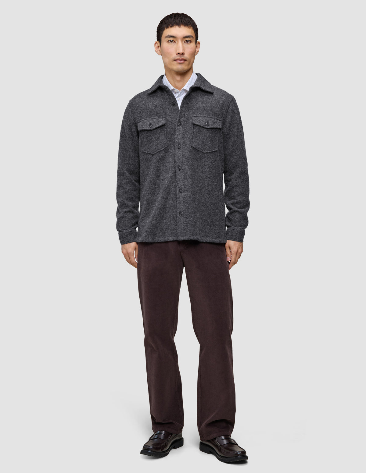 A man wearing a buttoned Double Layer Wool Overshirt Regular Dark Grey over a white collared shirt, paired with dark trousers and black loafers in a clean Scandinavian design.