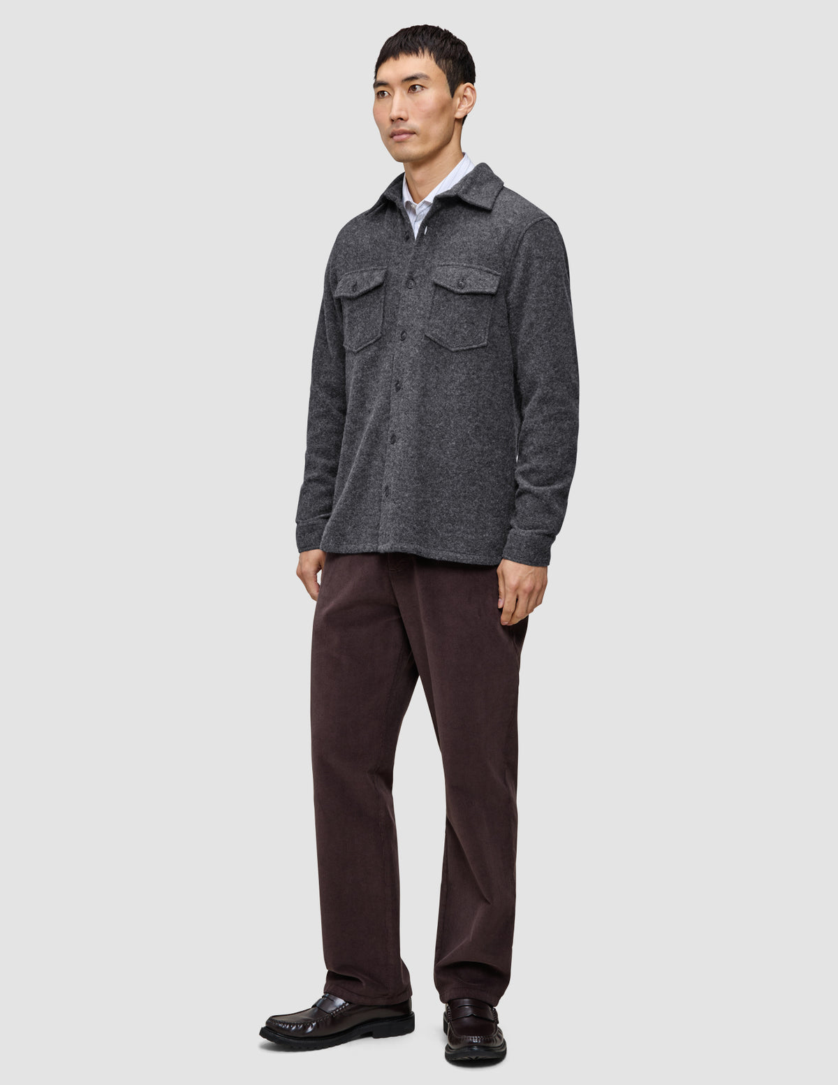 A man wears a Double Layer Wool Overshirt Regular Dark Grey over a white shirt, paired with dark brown trousers and dark loafers in a classic Scandinavian design.