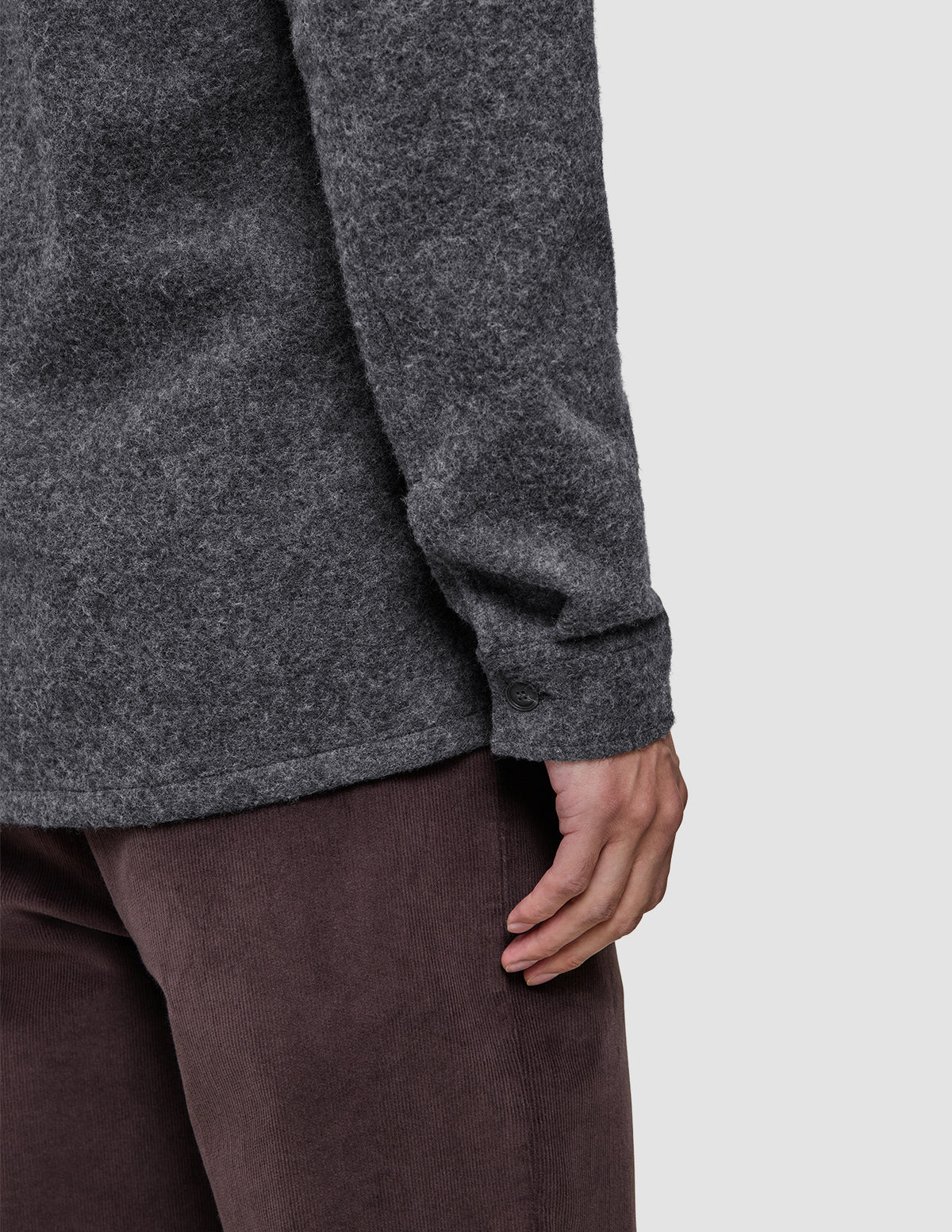 A person wearing a Double Layer Wool Overshirt Regular Dark Grey with long sleeves and brown trousers.
