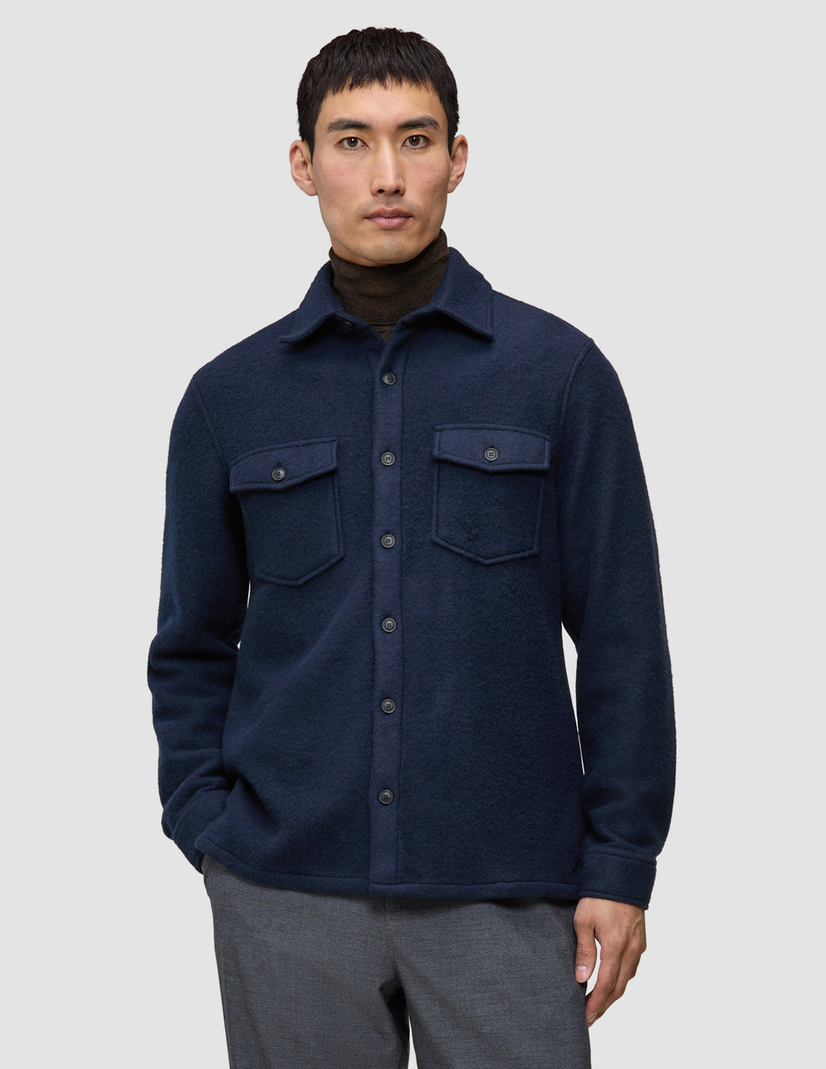A man wears a Double Layer Wool Overshirt Regular Dark Navy over a brown turtleneck, showcasing a clean Scandinavian design with two chest pockets.