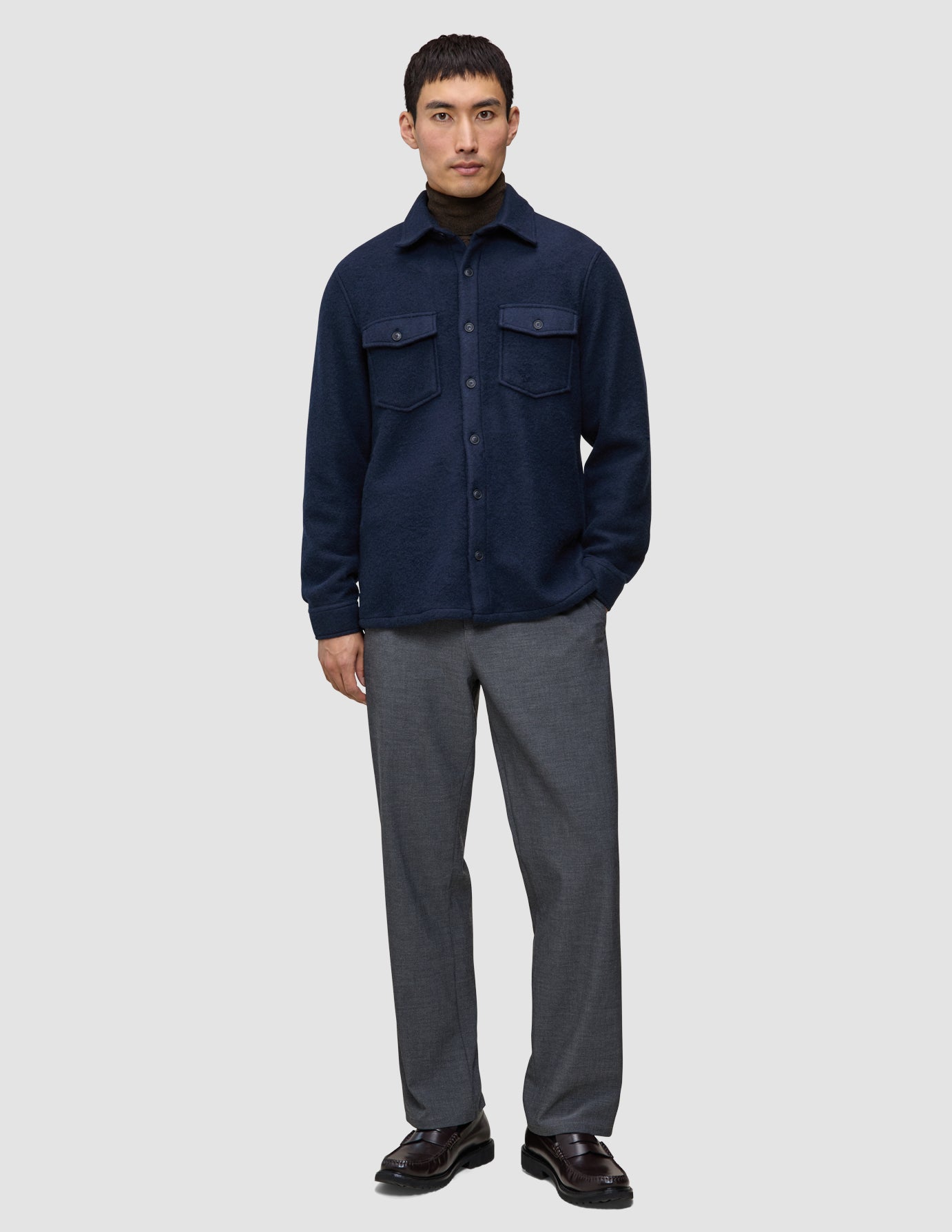 A man wears a Double Layer Wool Overshirt Regular Dark Navy over a brown turtleneck, paired with grey trousers and dark loafers.