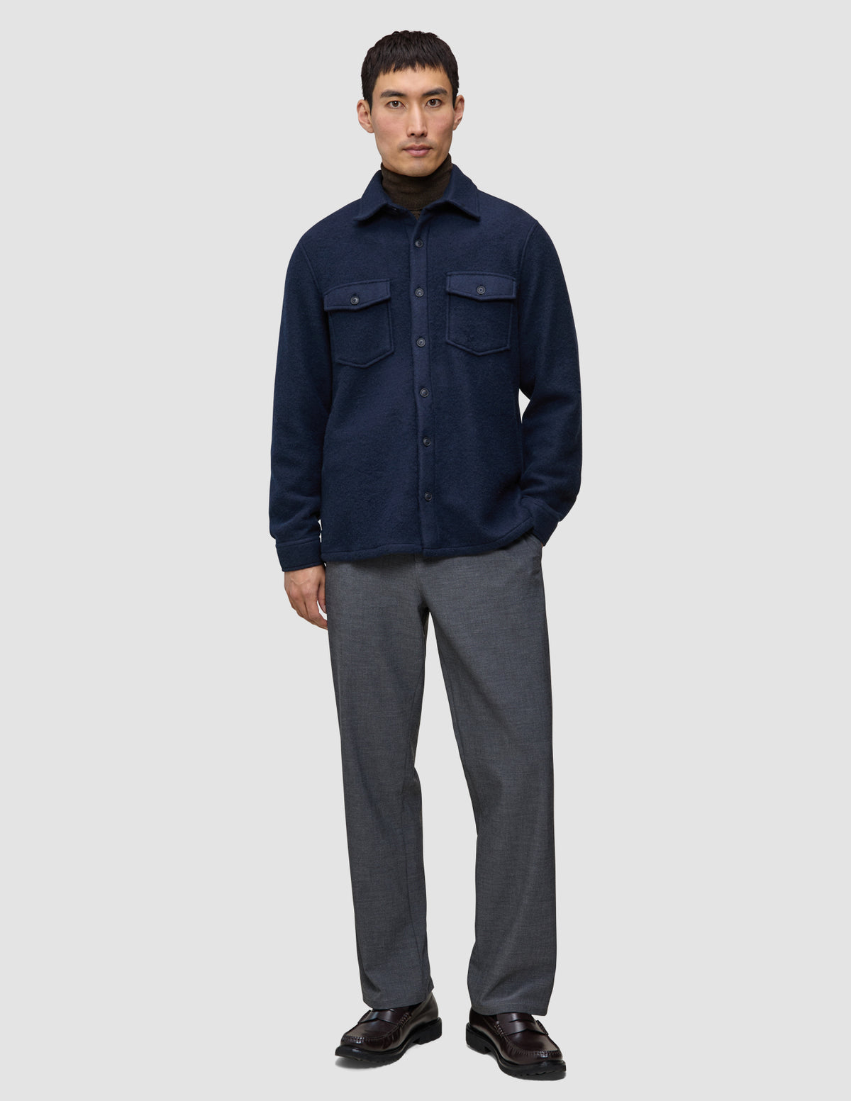 A man wears a Double Layer Wool Overshirt Regular Dark Navy over a brown turtleneck, paired with grey trousers and dark loafers.