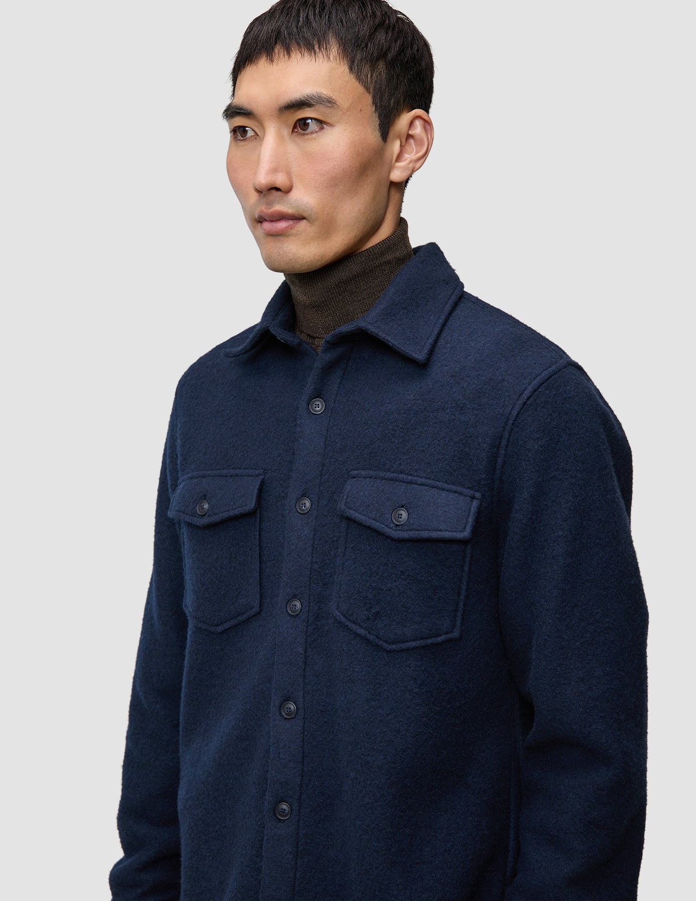 A man wearing a dark navy Double Layer Wool Overshirt Regular Dark Navy with two chest pockets over a dark brown turtleneck.