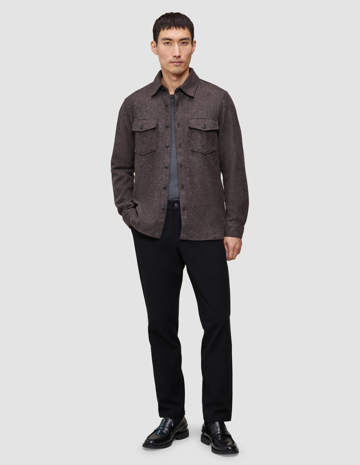 A man wearing a Double Layer Wool Overshirt Saddle Brown over a grey t-shirt, black trousers, and black loafers, reflecting a clean Scandinavian design.
