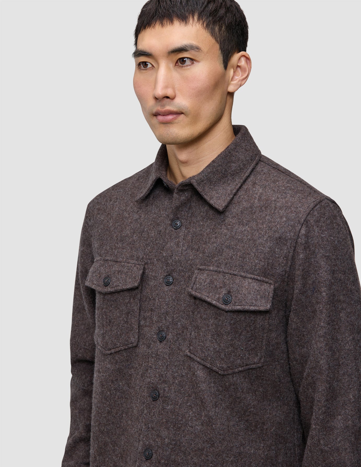 A man wears a brown Double Layer Wool Overshirt, featuring a button-up, double-layer design with two chest pockets with buttoned flaps.
