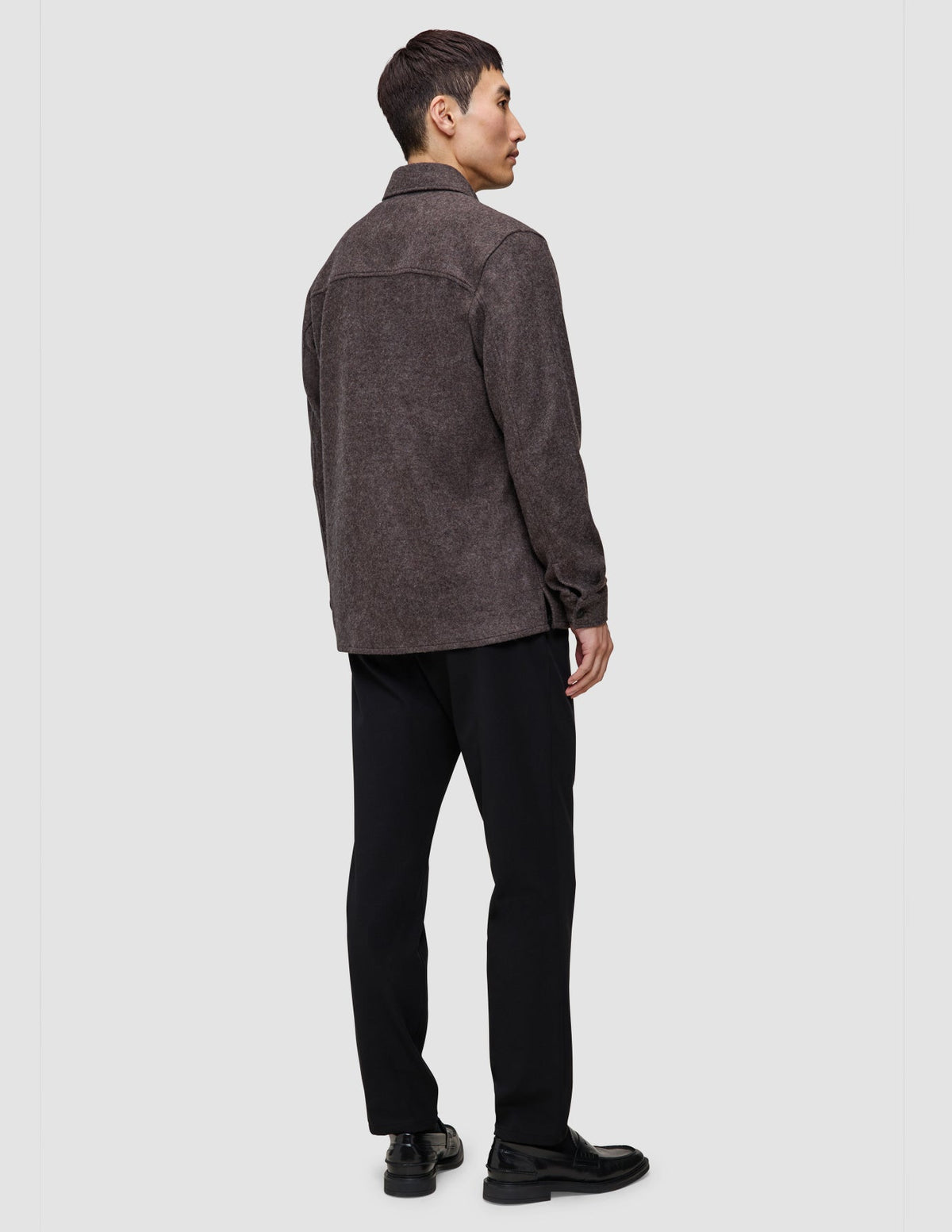 A person seen from behind wearing a Double Layer Wool Overshirt Saddle Brown, black trousers, and black loafers.