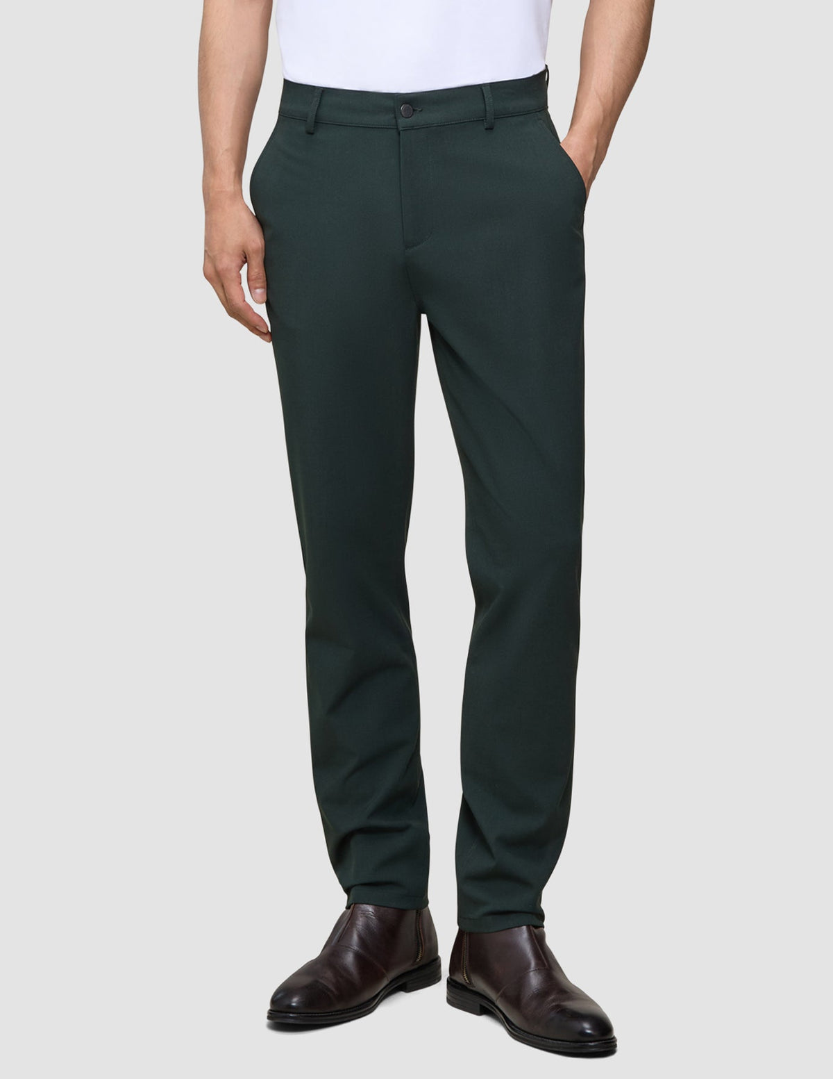 A person wears Ease Pants Regular Northern Pine dark green trousers and brown leather boots.