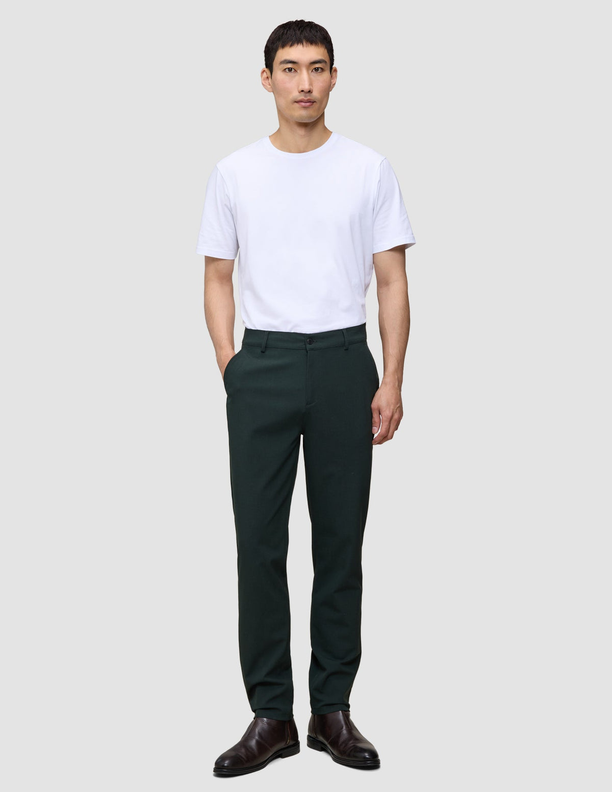 A person wearing a white t-shirt, Ease Pants Regular Northern Pine in dark green, and brown leather boots.