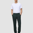 A man wearing a white t-shirt and dark green Ease Pants Regular Northern Pine with a tailored look, standing with his hands in his pockets.
