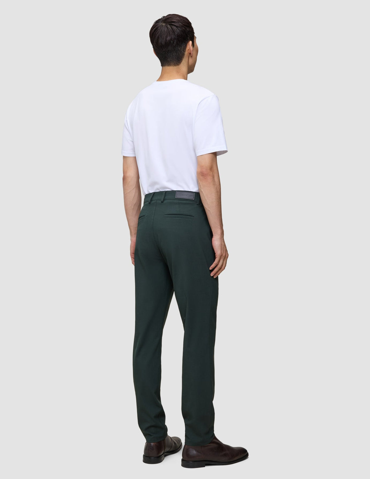A man seen from behind wearing a white t-shirt, Ease Pants Regular Northern Pine, and brown leather shoes.