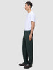 A person in profile wearing a white t-shirt, dark brown loafers, and Ease Pants Relaxed Fit Northern Pine, which are exceptionally soft, dark green, and relaxed-fit.