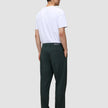 A man viewed from behind, wearing a white t-shirt and dark green Ease Pants Relaxed Fit Northern Pine with a tailored look, hands tucked into his pockets.