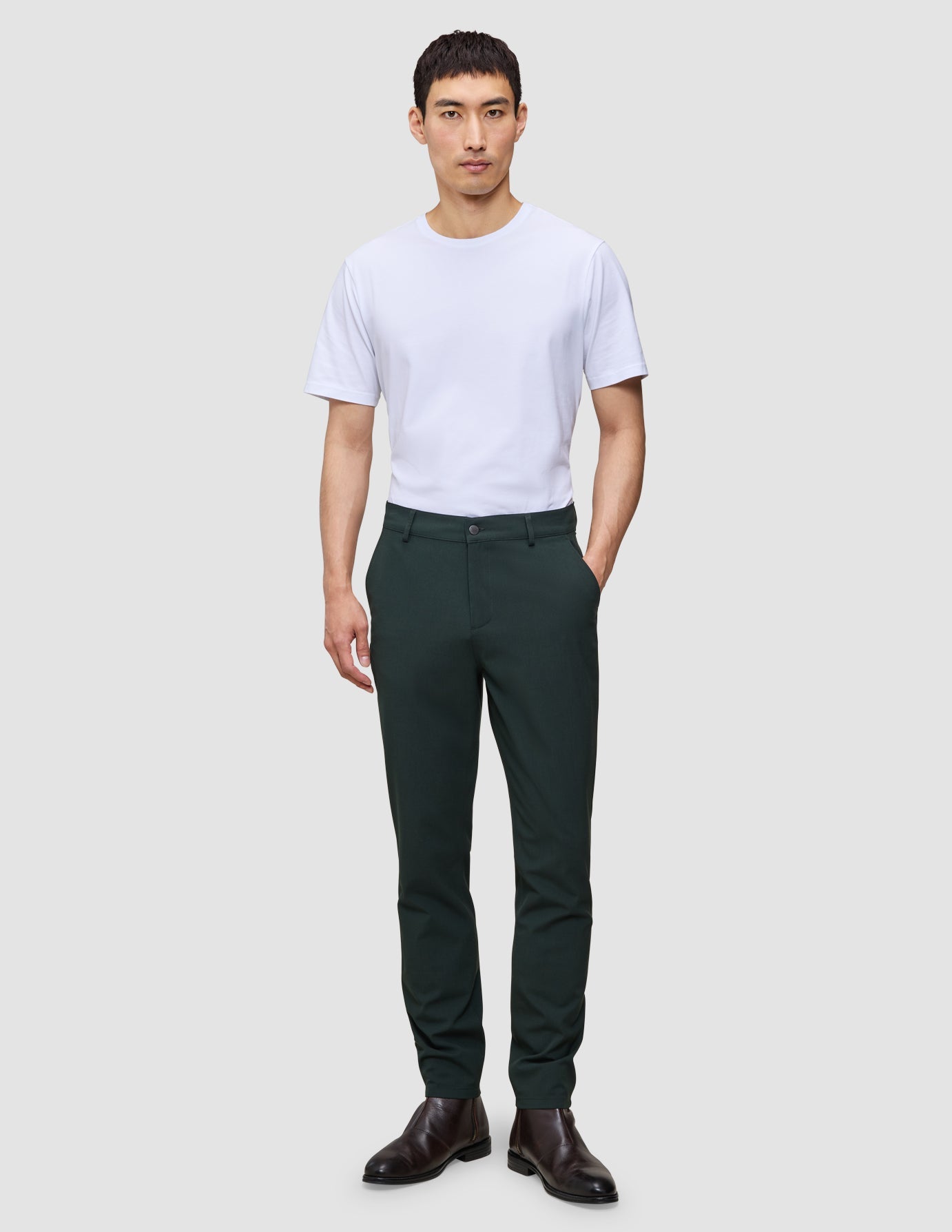 A man wearing a white t-shirt, Ease Pants Slim Northern Pine, and dark brown leather boots.