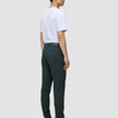 A person viewed from behind, wearing a white t-shirt, Ease Pants Slim Northern Pine, and dark leather boots.