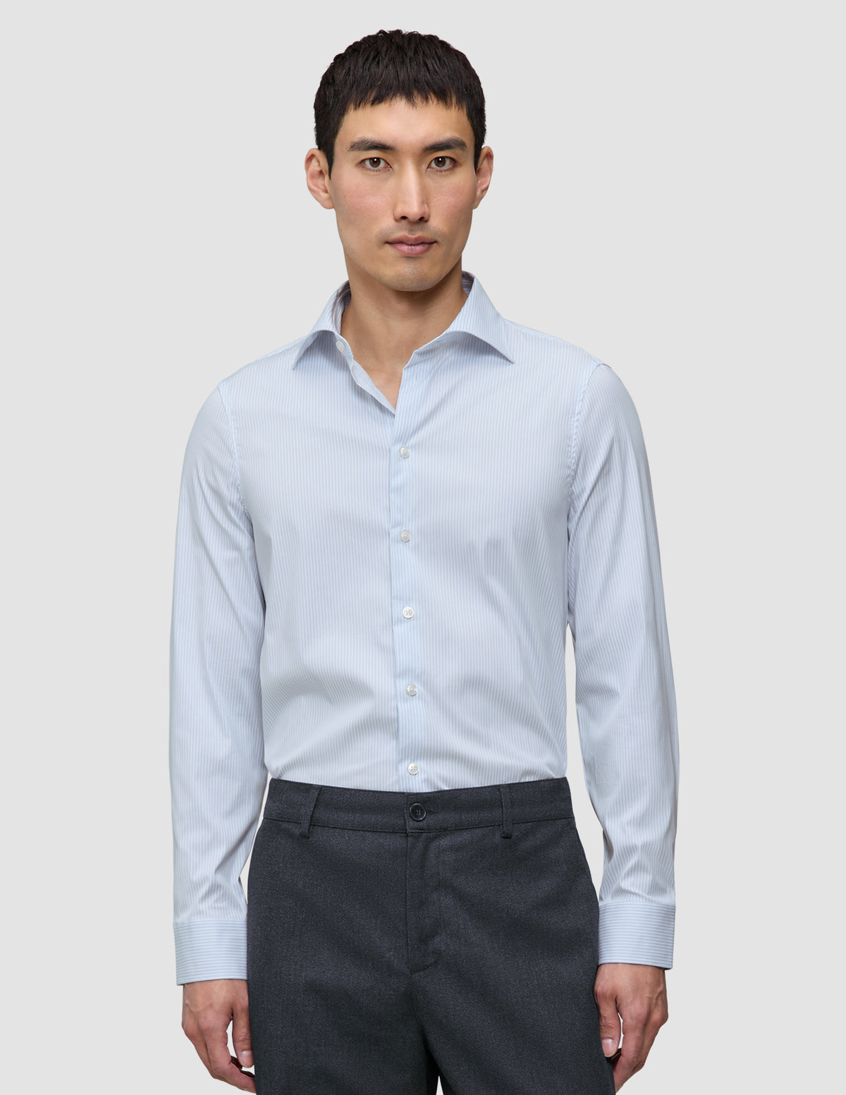 A man wearing an Elevated Shirt Regular Classic Blue Striped light blue and white pinstriped Pima cotton shirt tucked into dark grey trousers.