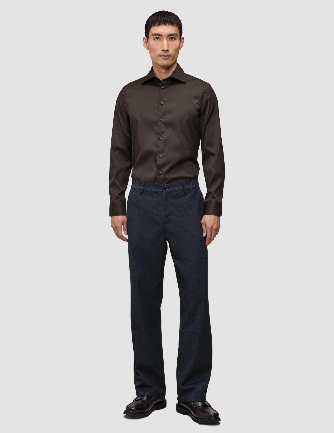 A man wearing an Elevated Shirt Regular Dark Brown tucked into dark trousers and brown loafers, reflecting a clean Scandinavian design aesthetic.