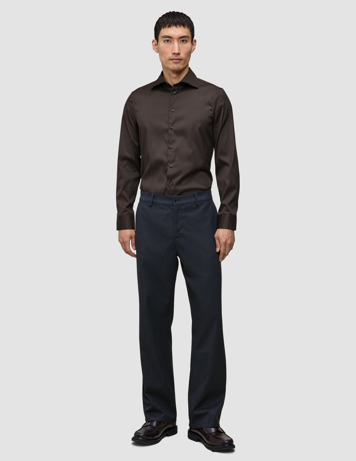 A man wearing an Elevated Shirt Regular Dark Brown tucked into dark trousers and brown loafers, reflecting a clean Scandinavian design aesthetic.