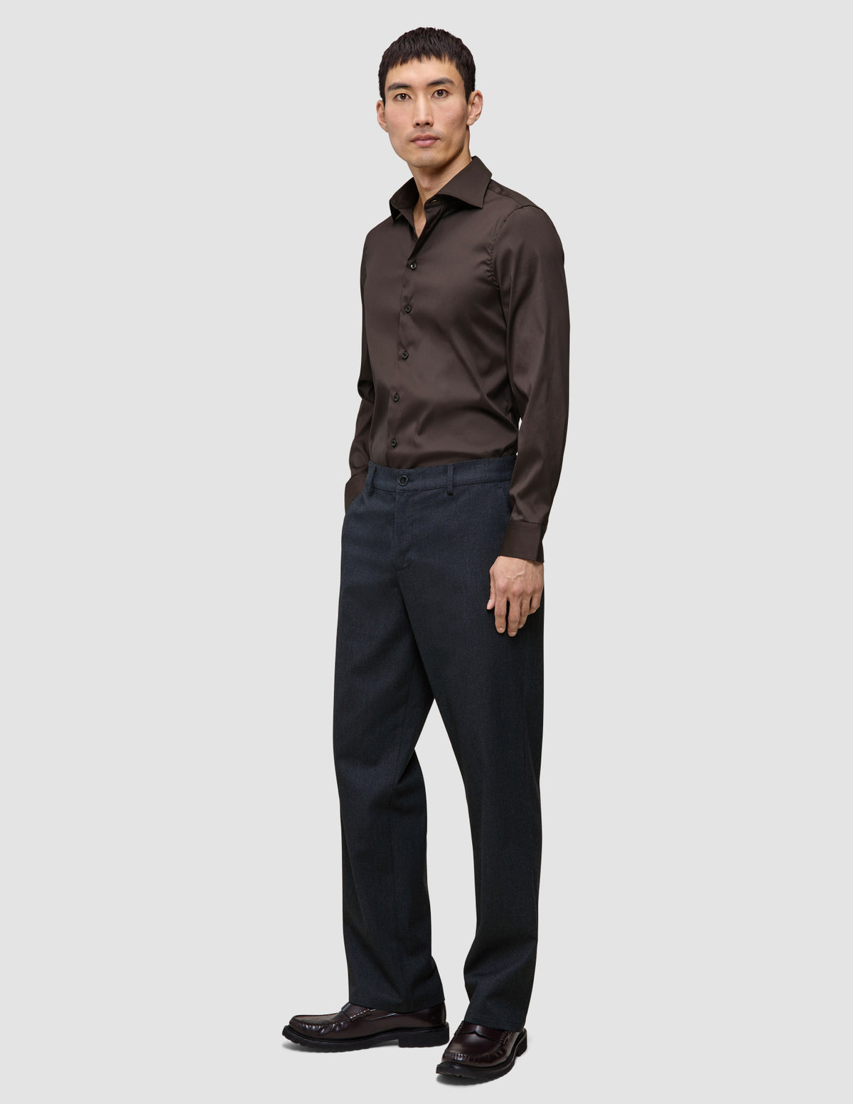 A man wearing an Elevated Shirt Regular Dark Brown long-sleeved button-down shirt and charcoal gray trousers.