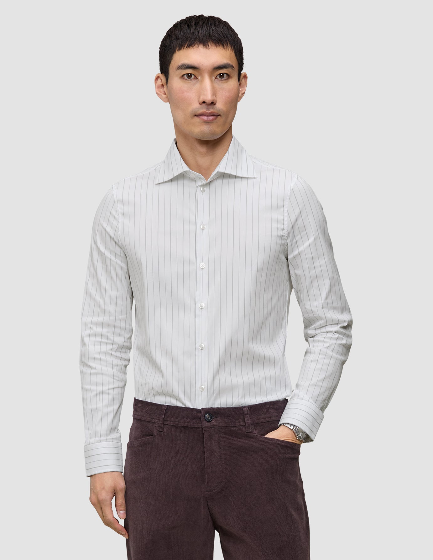 A man wearing an Elevated Shirt Regular Light Grey Striped long-sleeve pima cotton shirt tucked into dark brown pants.