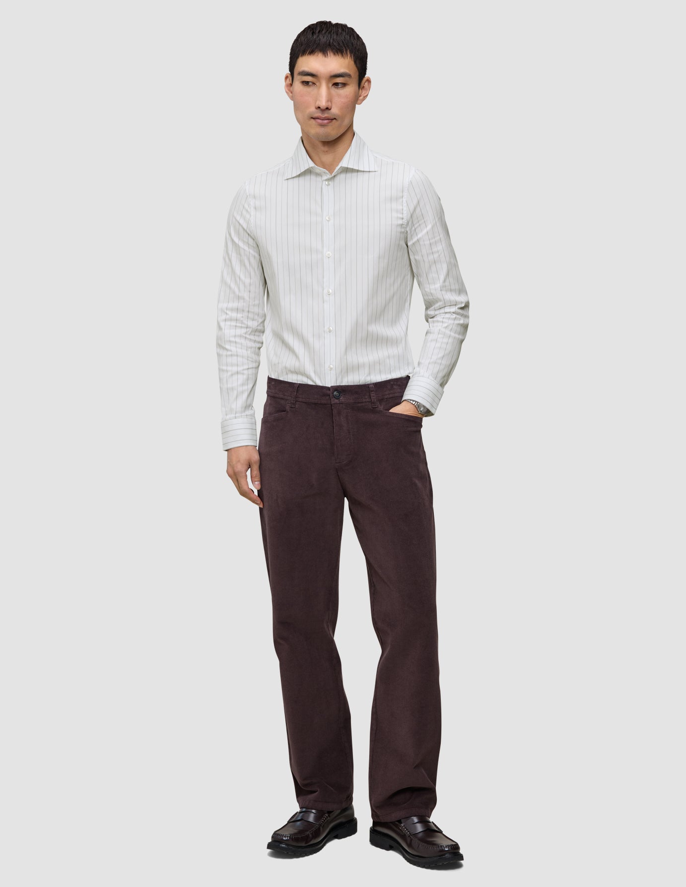 A man wearing an Elevated Shirt Regular Light Grey Striped button-up shirt, dark brown trousers, and black loafers.