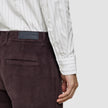 A person wearing an Elevated Shirt Regular Light Grey Striped in thin grey vertical stripes and dark brown corduroy trousers.