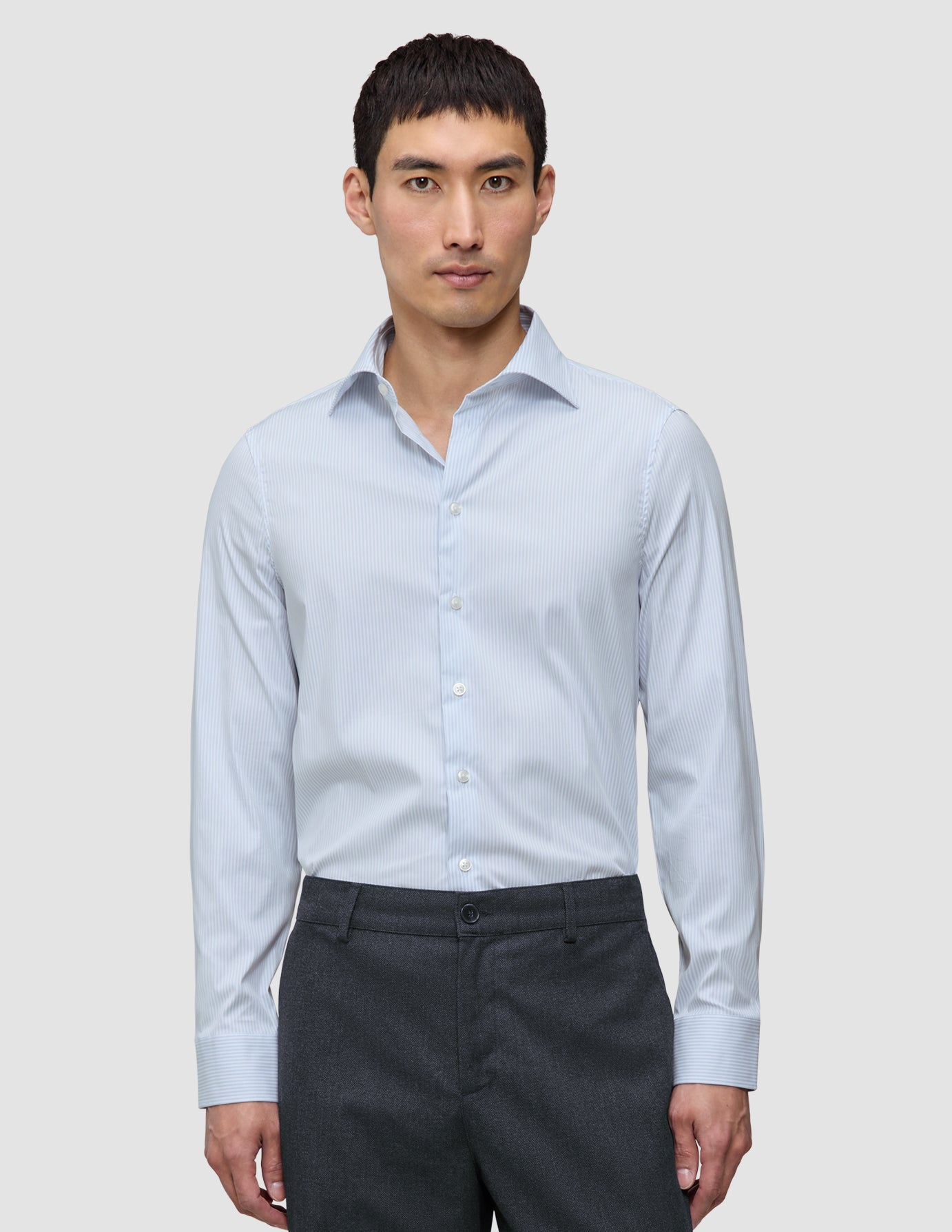 A man wearing an Elevated Shirt Slim Classic Blue Striped long-sleeve dress shirt tucked into dark grey trousers.