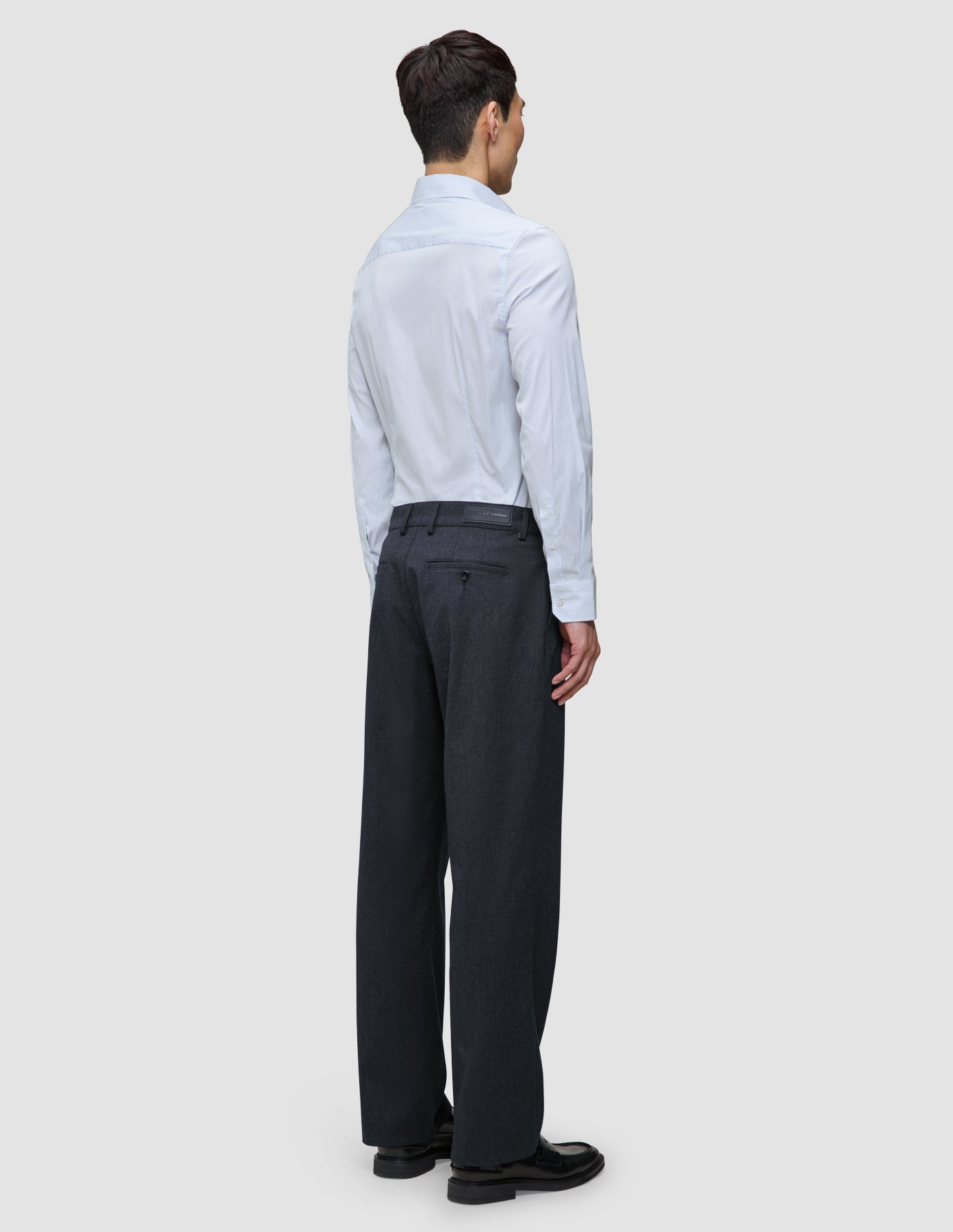 A man seen from behind wearing an Elevated Shirt Slim Classic Blue Striped light blue pinstripe long-sleeve shirt tucked into dark grey trousers and black loafers.