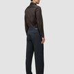 A man stands facing away, wearing an Elevated Shirt Slim Dark Brown tucked into charcoal grey trousers and dark brown shoes.