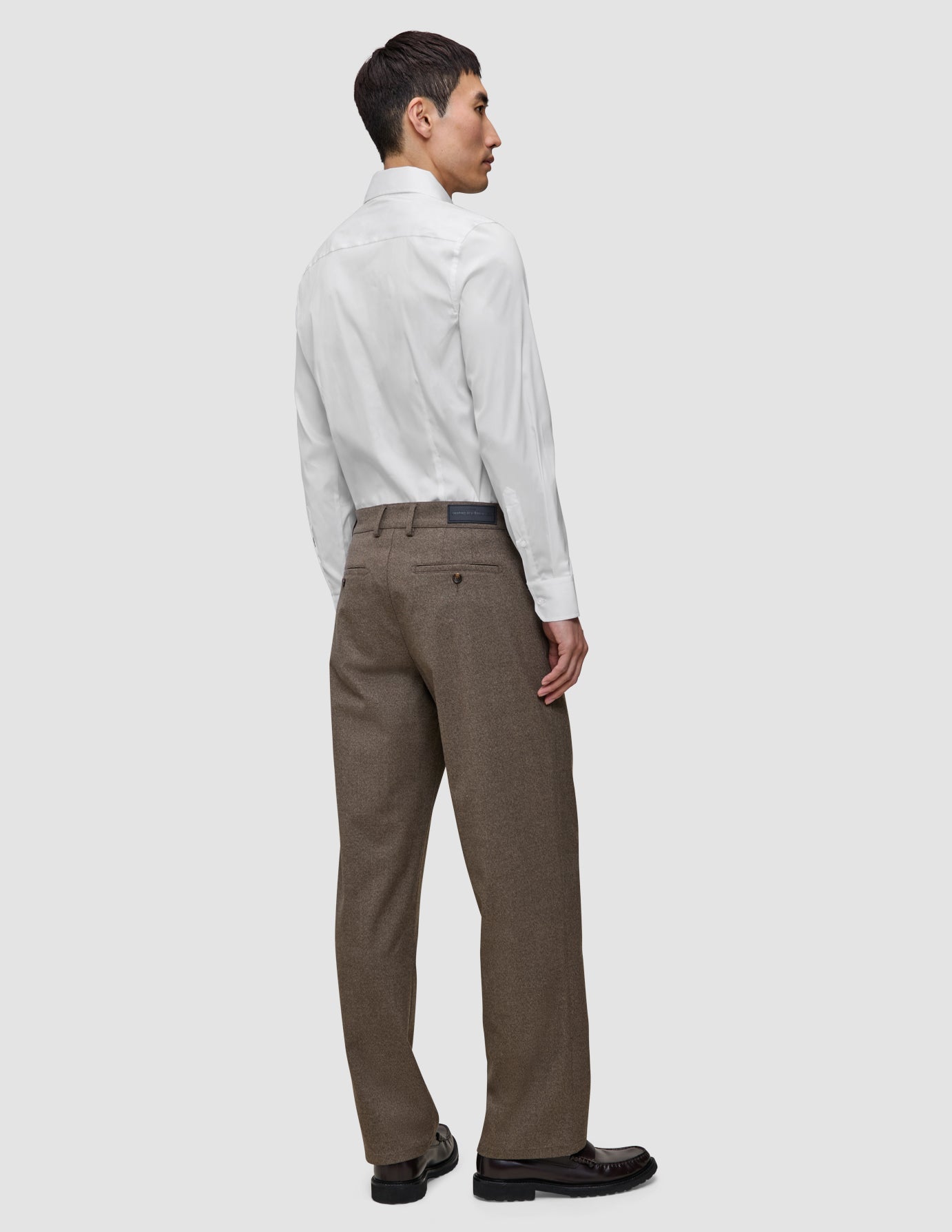 A man seen from behind wearing an Elevated Shirt White Slim tucked into brown trousers and dark loafers.