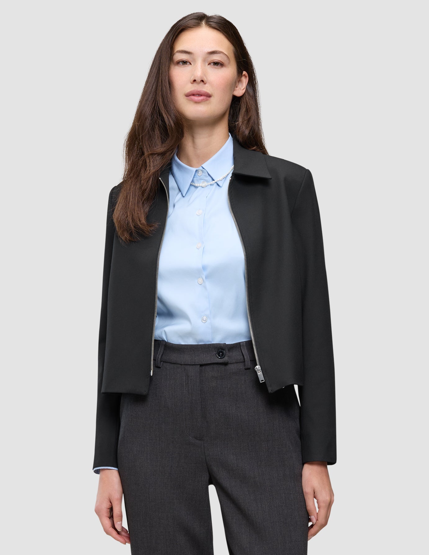 A woman wearing a black Essential Short Zip Jacket over a light blue button-down shirt.