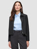 A woman wearing a black Essential Short Zip Jacket over a light blue button-down shirt.