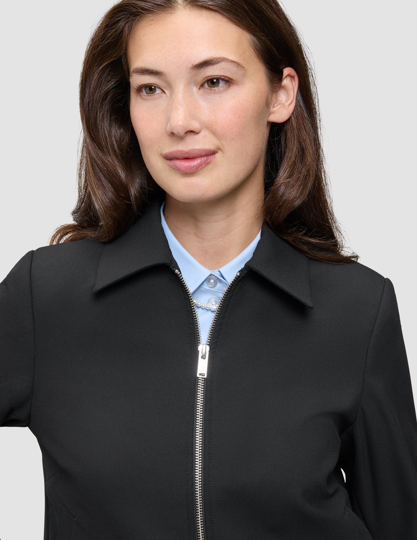 A minimalist black Essential Short Zip Jacket worn over a light blue button-down shirt.