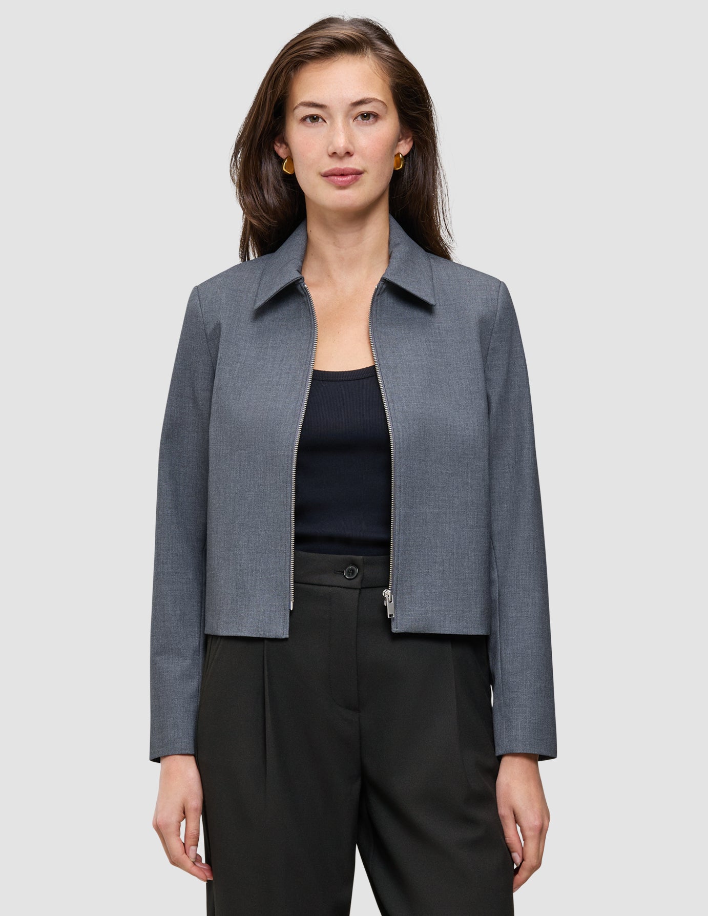 A person wears an Essential Short Zip Jacket Dark Grey Melange over a black top and trousers, showcasing a minimalist blazer aesthetic.
