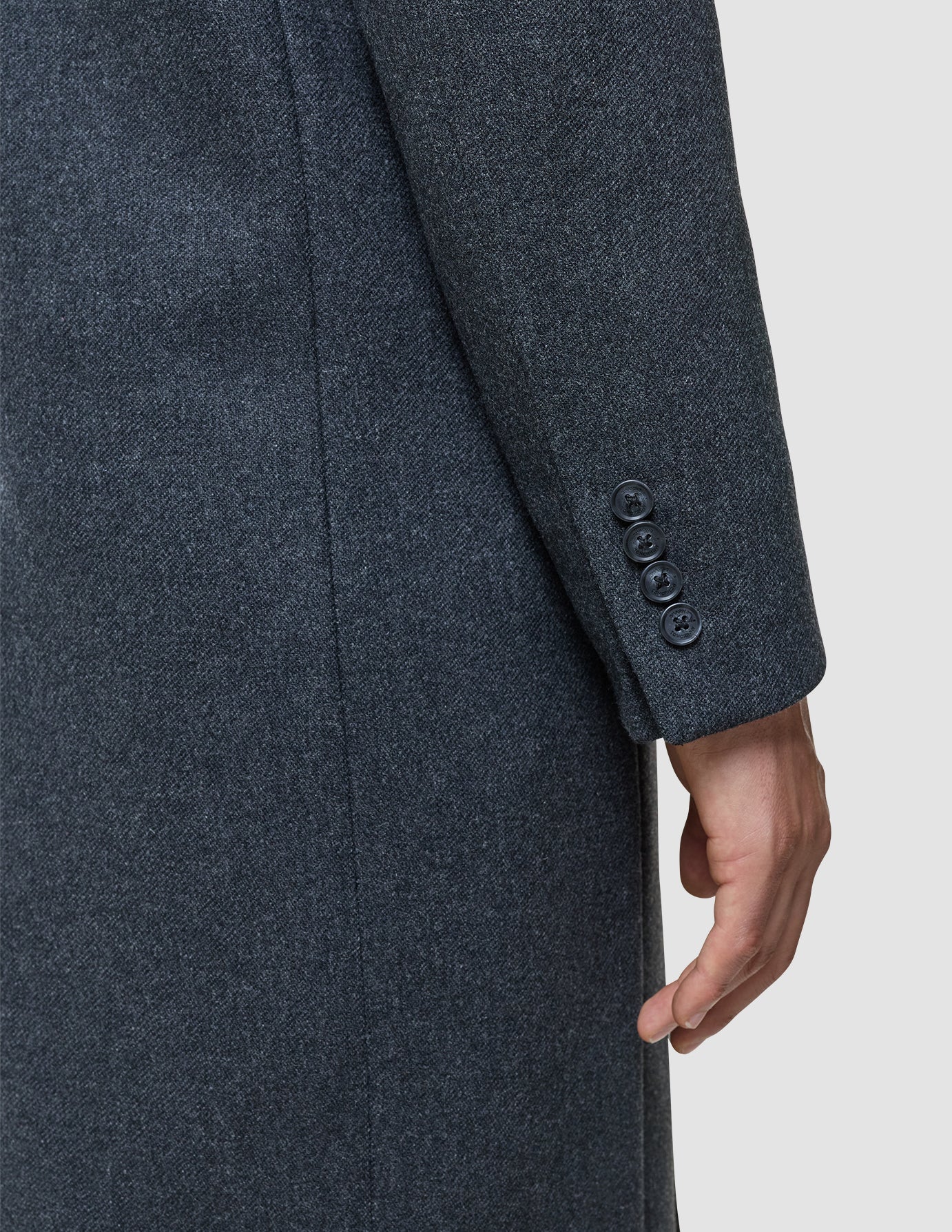 A dark grey Maxi Wool Coat sleeve showing four buttons on the cuff with a person’s hand at their side.